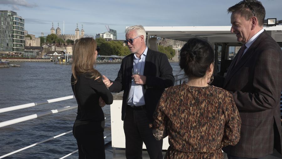 A group of guests in conversation on deck with the Tower of London across the water